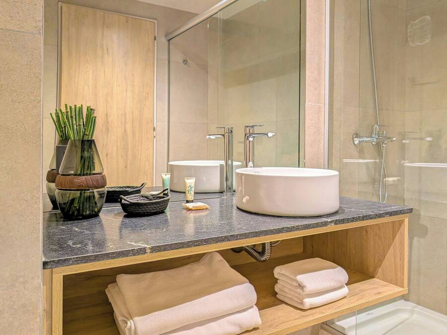 A modern bathroom with a glass shower enclosure, a marble countertop, and a wooden vanity with towels.