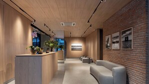 A reception area with a wooden reception desk, seating area, and a brick wall with framed pictures. - Brickton, Rosario, Apartments By Marriott Bonvoy (Rosario)