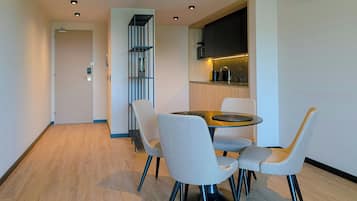Un comedor moderno con una mesa redonda, cuatro sillas grises, una cocina integrada con microondas y un estante vertical.