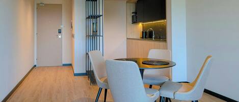 A modern dining area with a round table, four grey chairs, a built-in kitchen with a microwave, and a vertical shelving unit.