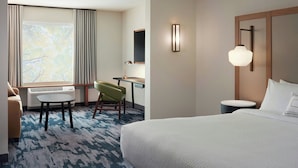 Habitación de hotel con cama, escritorio, silla, mesita, lámpara y ventana con cortinas.