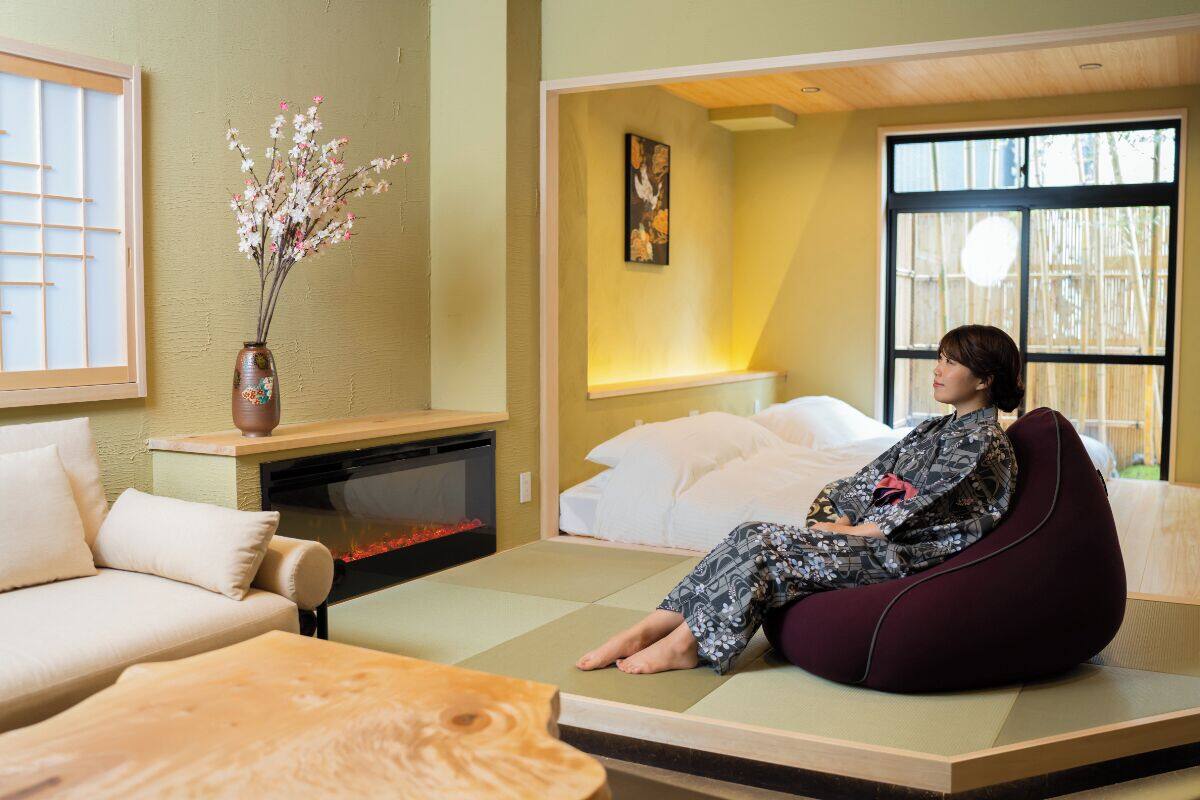 A room with a bed, a sofa, a wooden table, a vase with flowers, and a painting on the wall.