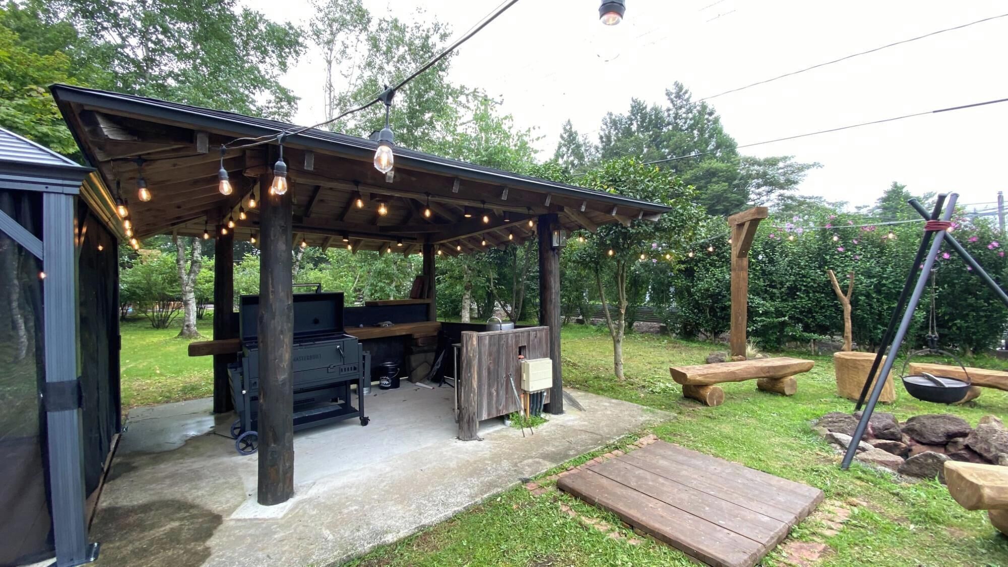 Patio esterno con barbecue, sedute in legno e luci decorative.