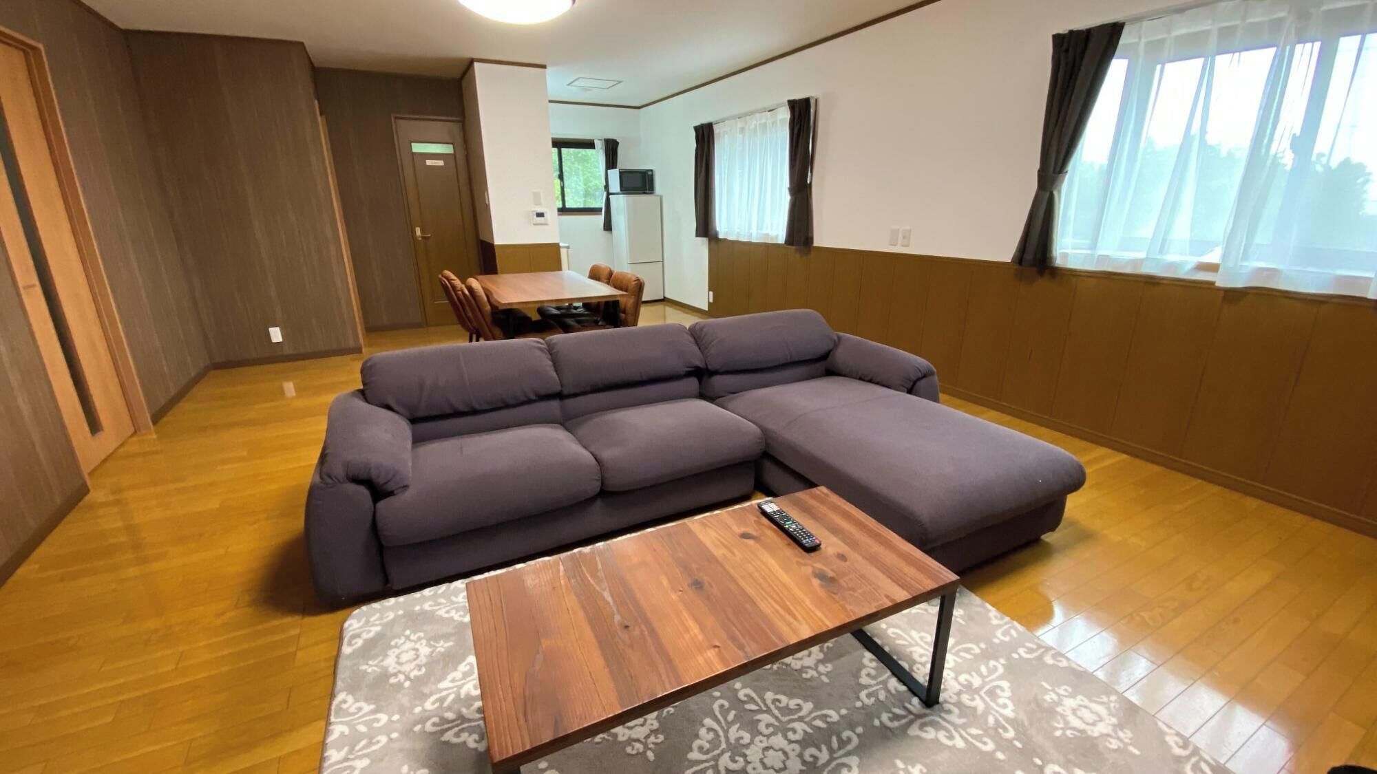 A living room with a sectional sofa, a wooden coffee table, and a dining area in the background.