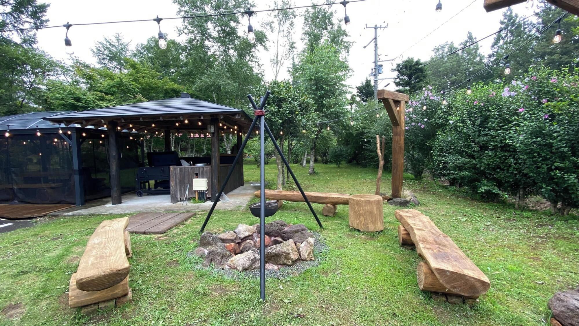 An outdoor patio area with a covered seating area, a fire pit, wooden benches, and string lights.