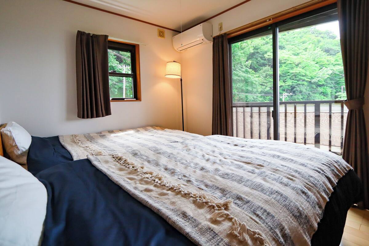 A bedroom with a bed, a window, a lamp, and a view of greenery.