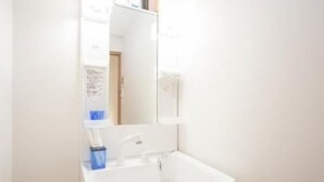 A bathroom with a white sink, a mirror, and a blue toothbrush holder. - Enraku (Kyoto)