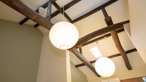 A room with exposed wooden beams, a hanging light fixture, and a ceiling light. - Enraku (Kyoto)