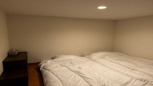 Ein kleiner, schlicht eingerichteter Raum mit einem Bett, einem Nachttisch und einem kleinen Tisch.