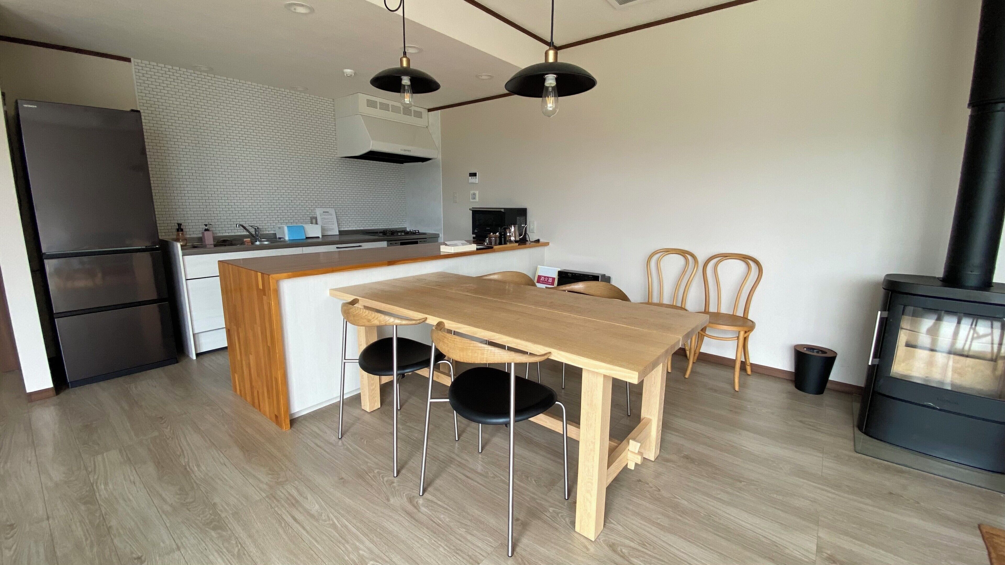 A modern kitchen with a wooden dining table, chairs, a built-in stove, and a refrigerator.
