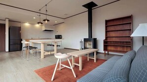 A modern living room with a sofa, a wooden table, a bench, a fireplace, and a bookshelf.