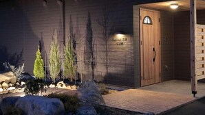 A building with a wooden exterior, a door with a window, and a small garden with rocks and plants.