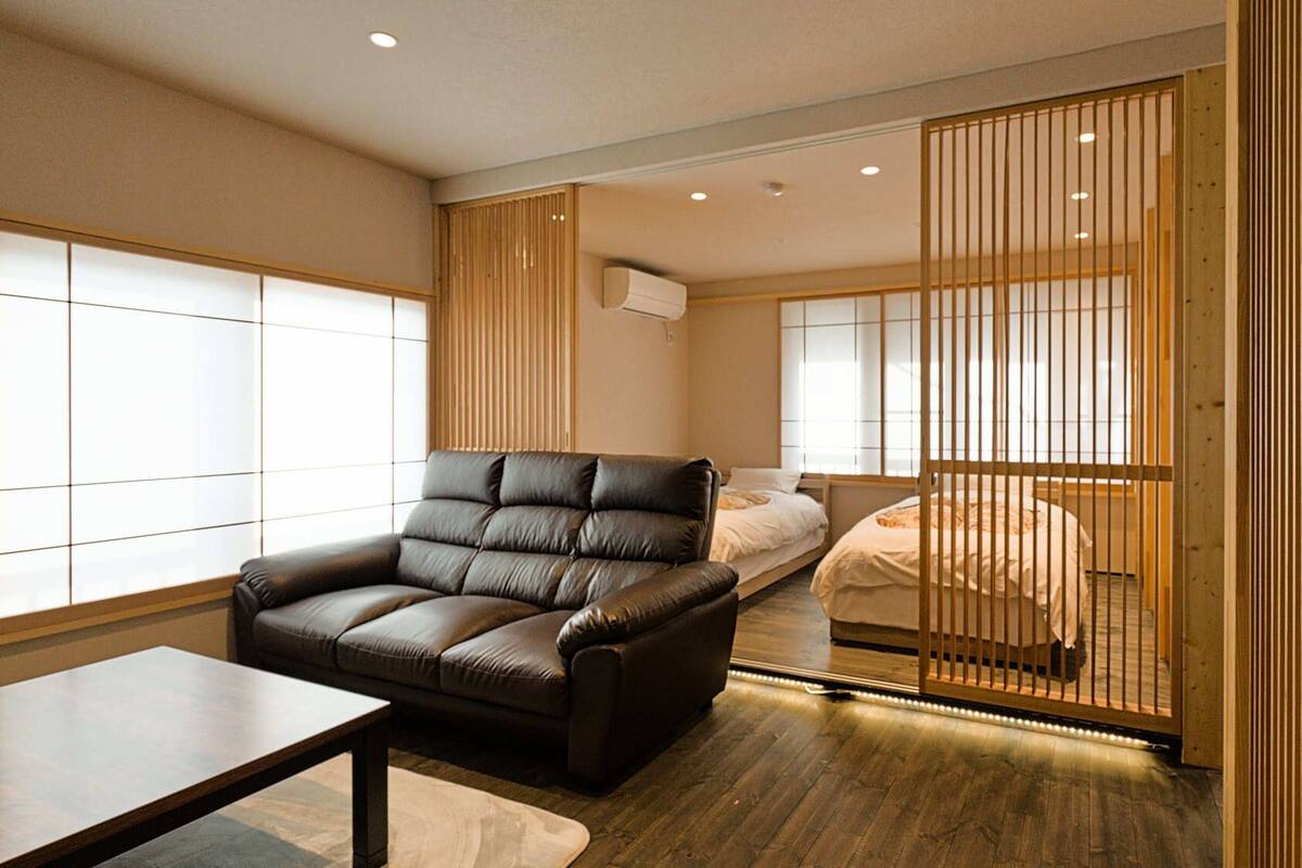 Ein modernes Hotelzimmer mit einer Ledersofa, einem Bett, einer verschiebbaren Shoji-Schirmwand und Blick auf die Stadt.