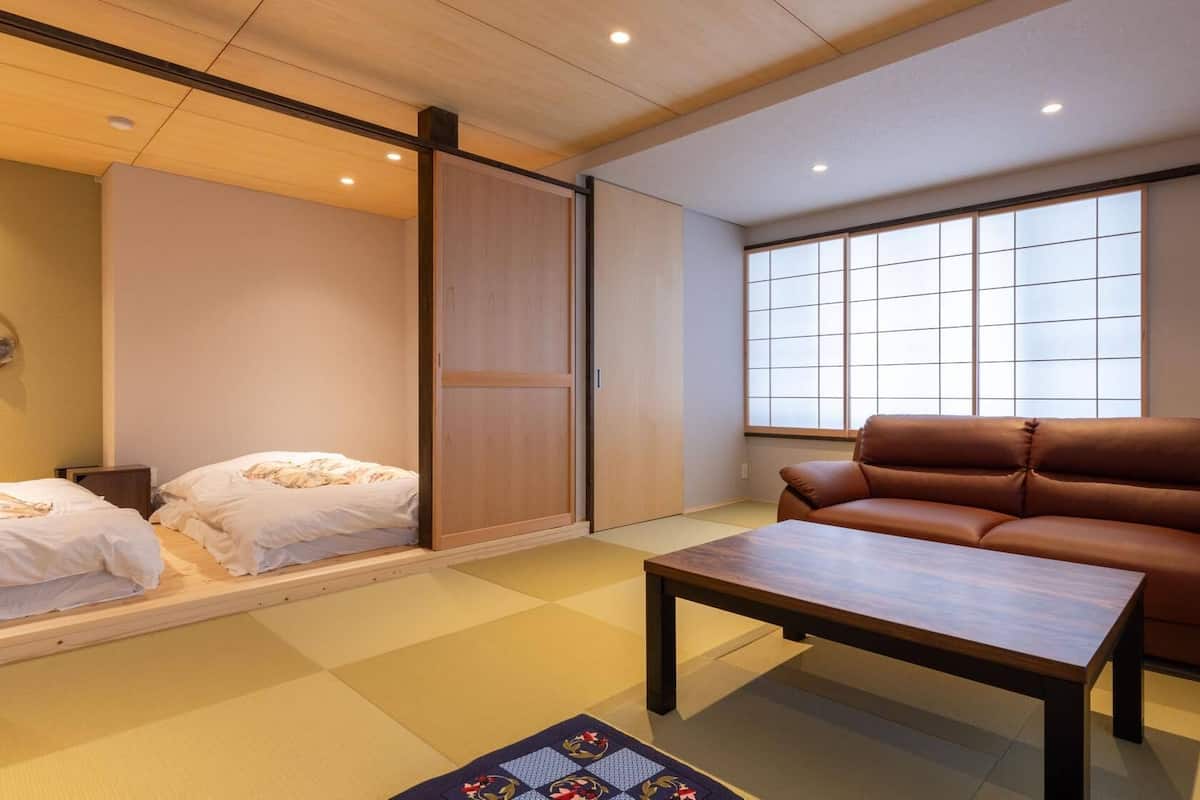 Ein Zimmer mit Tatami-Matten, einem braunen Ledersofa, einem Holztisch und einer Schiebetür.