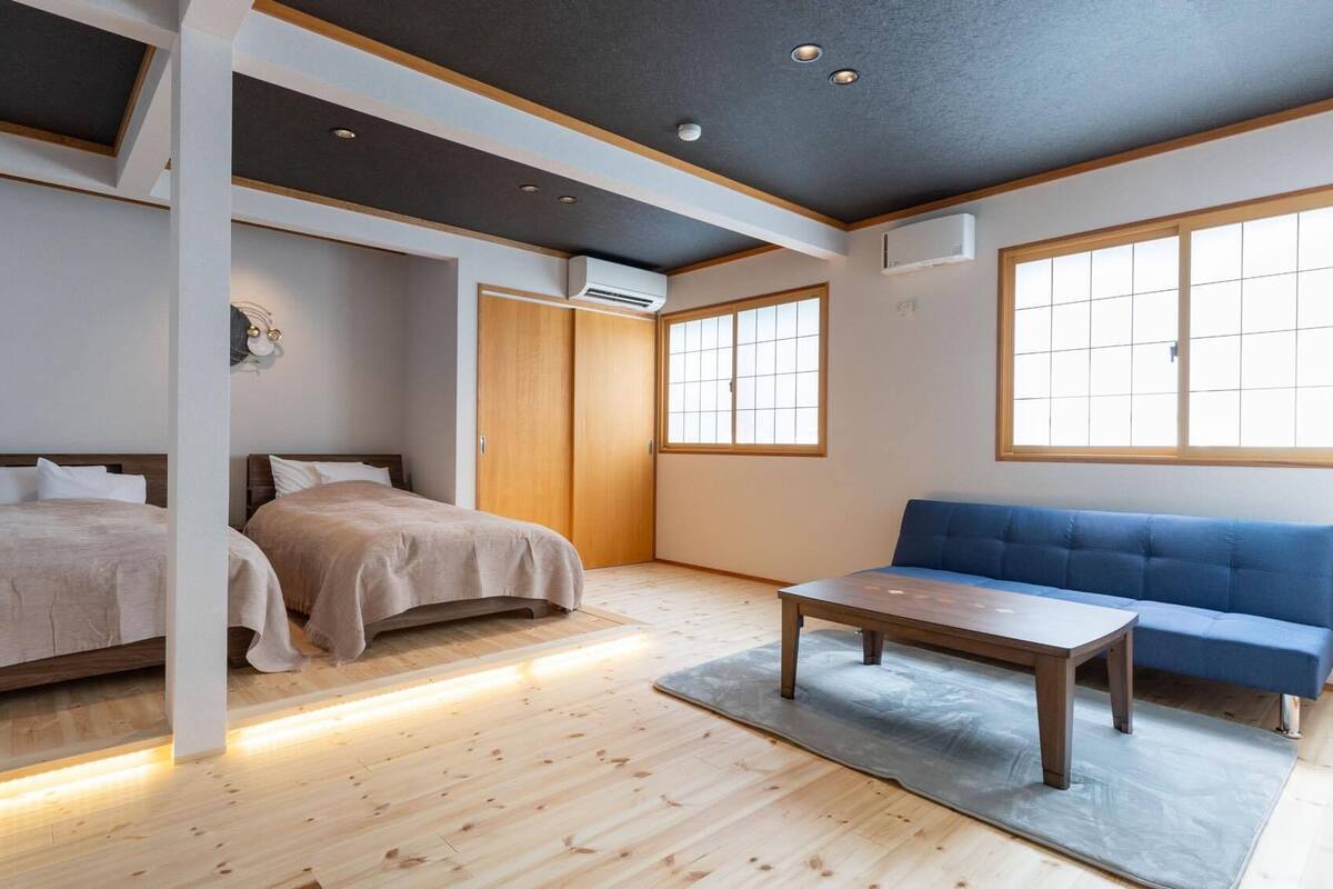 Ein Zimmer mit zwei Betten, einem blauen Sofa, einem Holztisch und großen Fenstern.