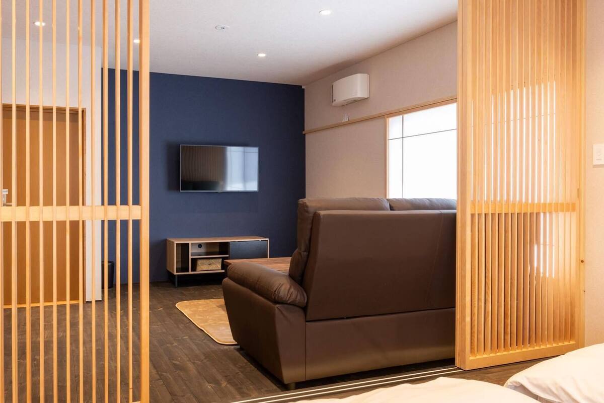 Ein modernes Zimmer mit einem braunen Sofa, einem an der Wand montierten Fernseher und einer Holzwand.