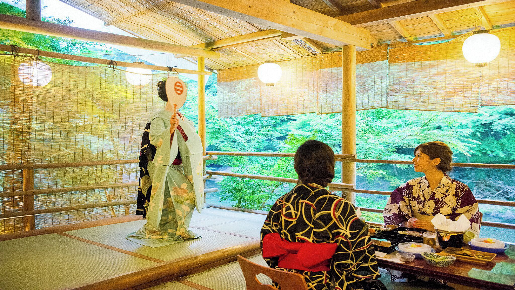 Un décor japonais traditionnel avec un sol recouvert de tatamis, un plafond en bois et une vue sur une végétation luxuriante.