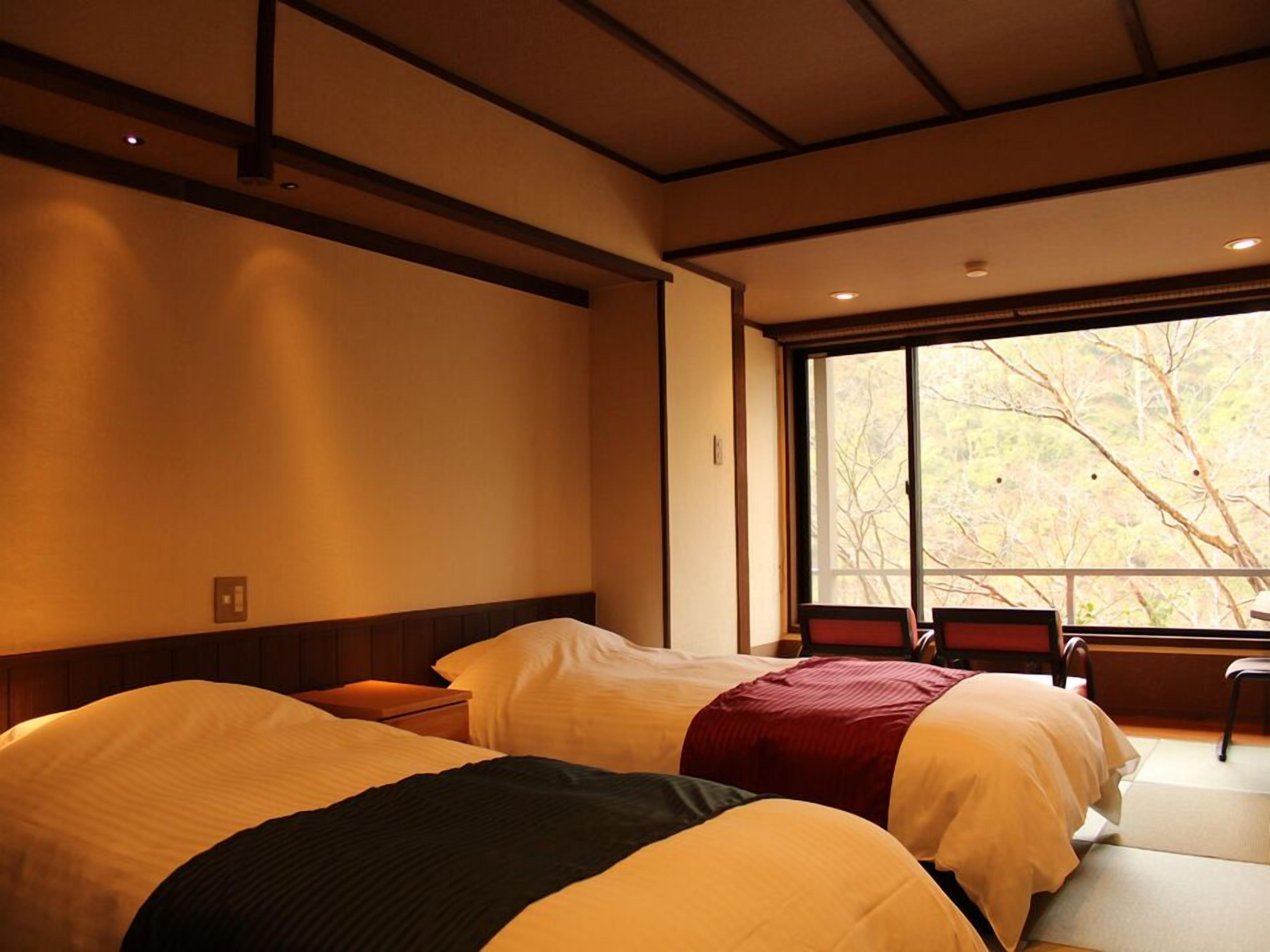 A hotel room with two beds, a window with a view of trees, and a wooden ceiling.