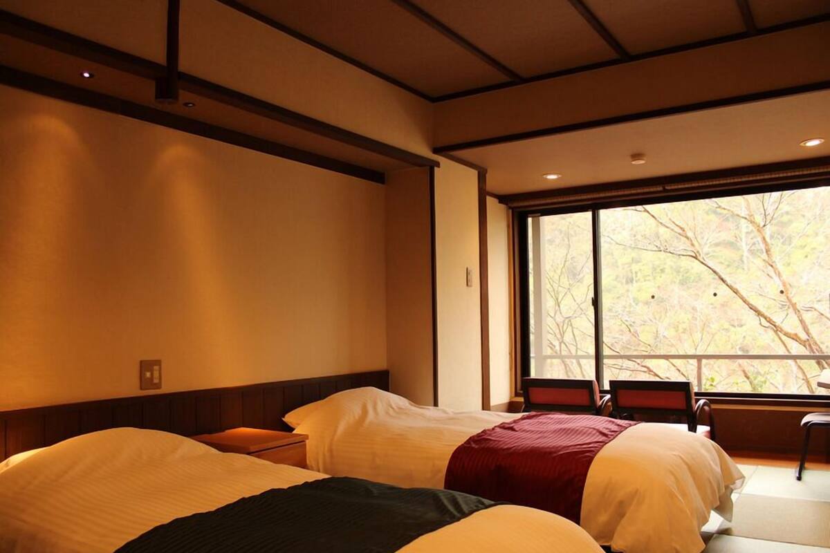A hotel room with two beds, a window with a view of trees, and a wooden ceiling.