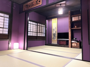 Um espaço com tatames, porta deslizante, divisória japonesa e televisão sobre suporte de madeira.