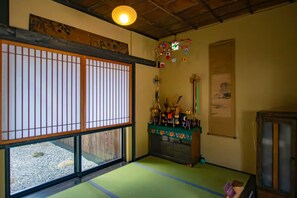Une pièce traditionnelle japonaise avec un sol recouvert de tatamis, des paravents en papier de riz (shoji), un futon servant de lit, un petit autel orné de divers objets et un meuble en bois.