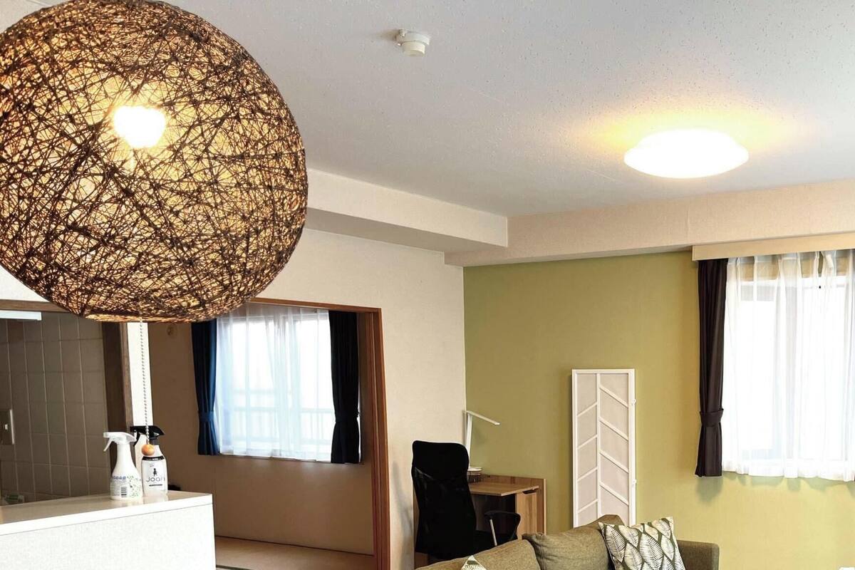 Uma sala de estar com uma luminária trançada grande, uma TV de tela plana, um sofá e uma escrivaninha com uma cadeira.