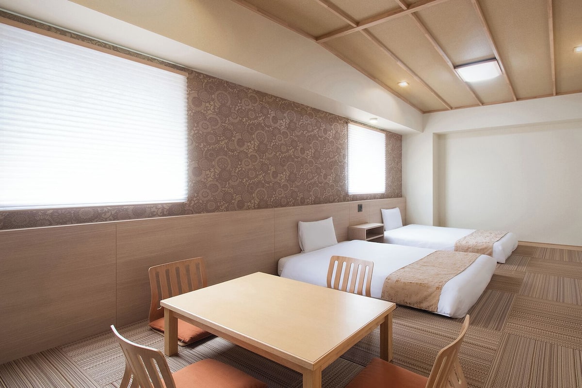 A hotel room with a wooden ceiling, two beds, a table, and chairs.