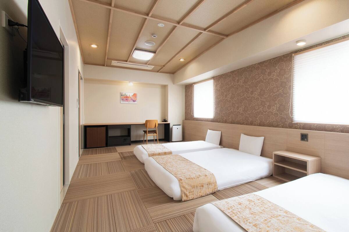 A hotel room with two beds, a desk, a chair, a TV, and a window.
