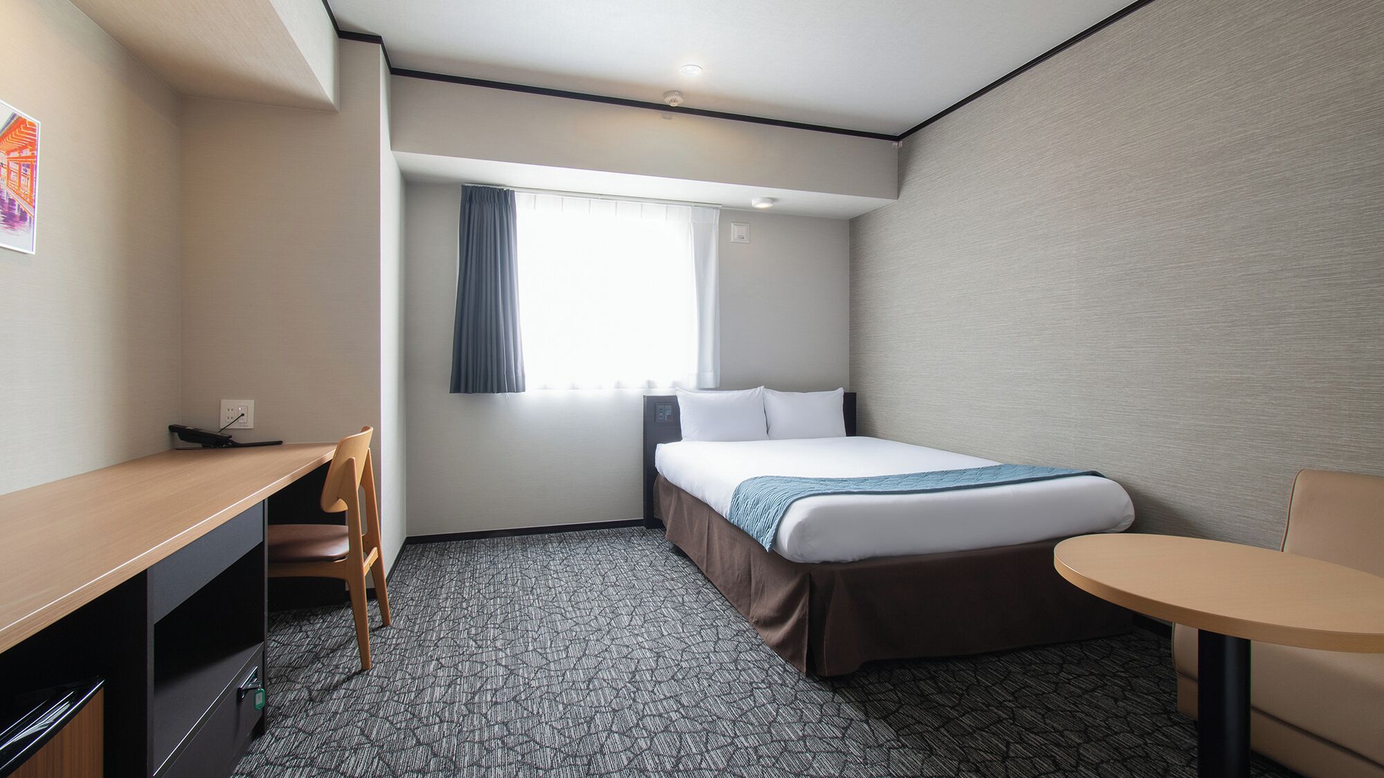 Ein Hotelzimmer mit Bett, Schreibtisch, Stuhl und einem kleinen Tisch.