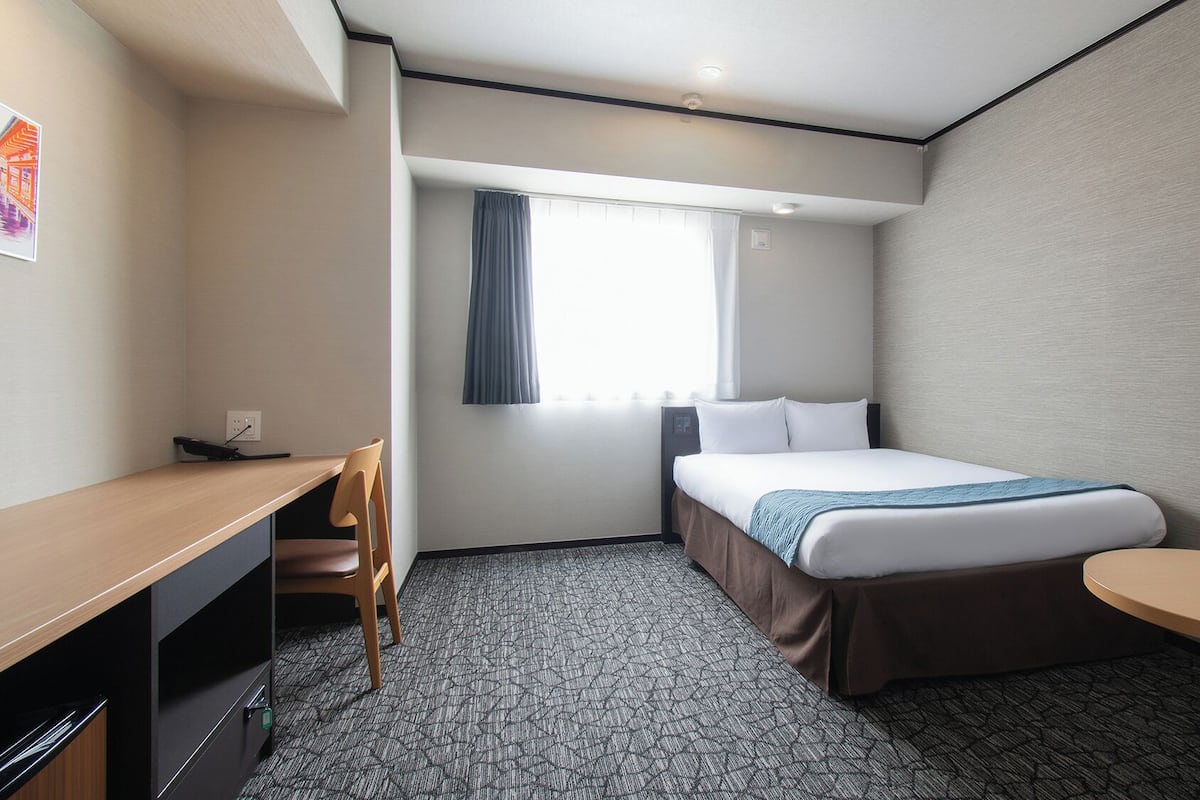 A hotel room with a bed, desk, chair, and a small table.
