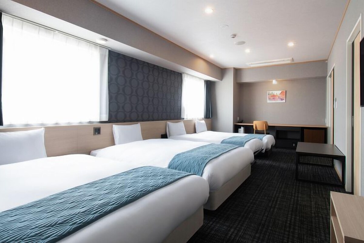 Habitación de hotel con tres camas, un escritorio, una silla y un televisor.