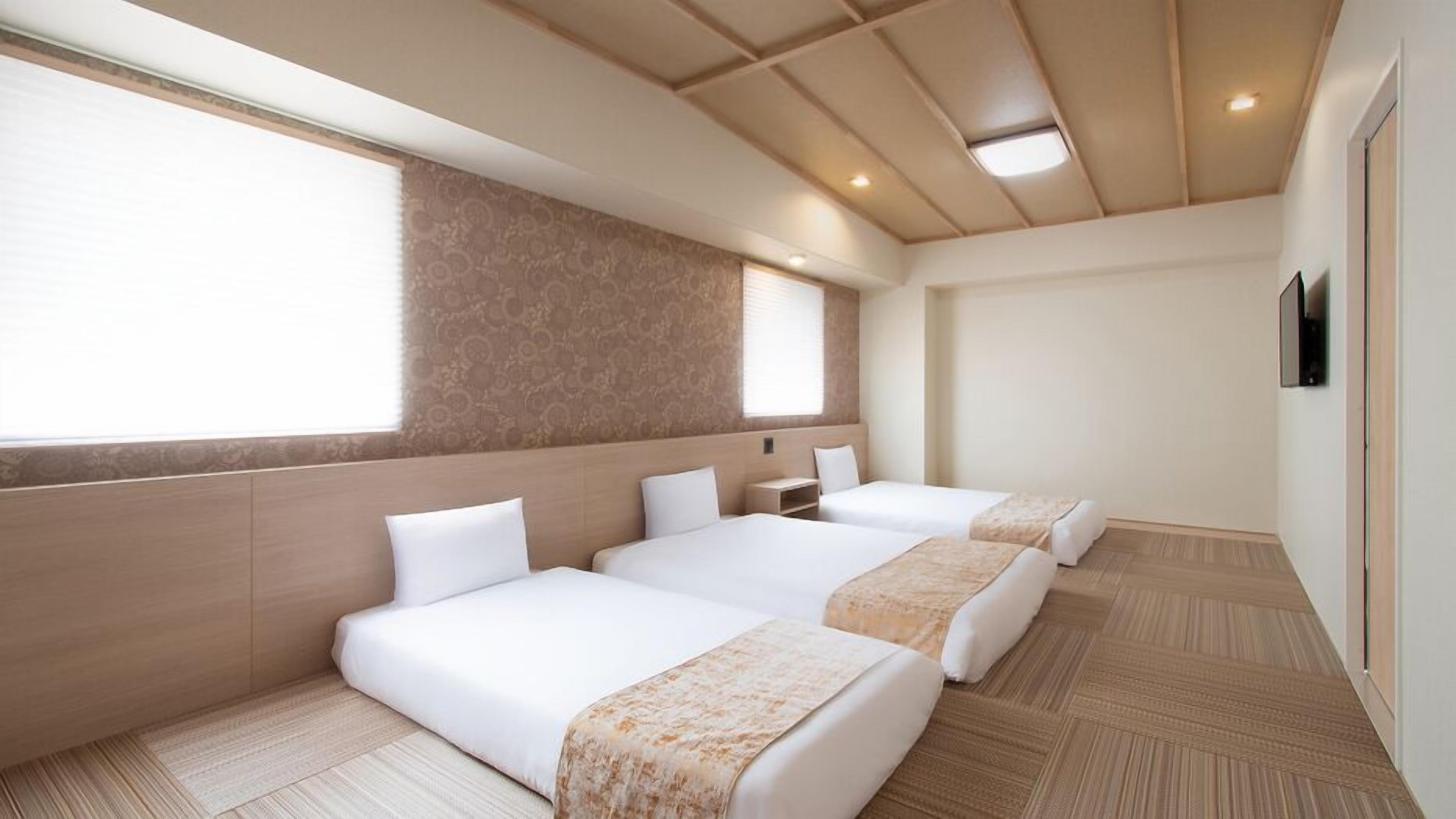 Ein Hotelzimmer mit drei Betten, einem großen Fenster und einer Holzbalkendecke.