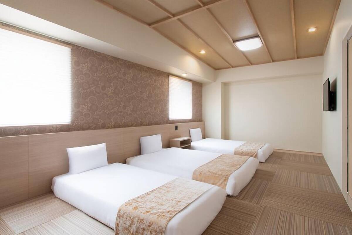 A hotel room with three beds, a large window, and a wooden ceiling.
