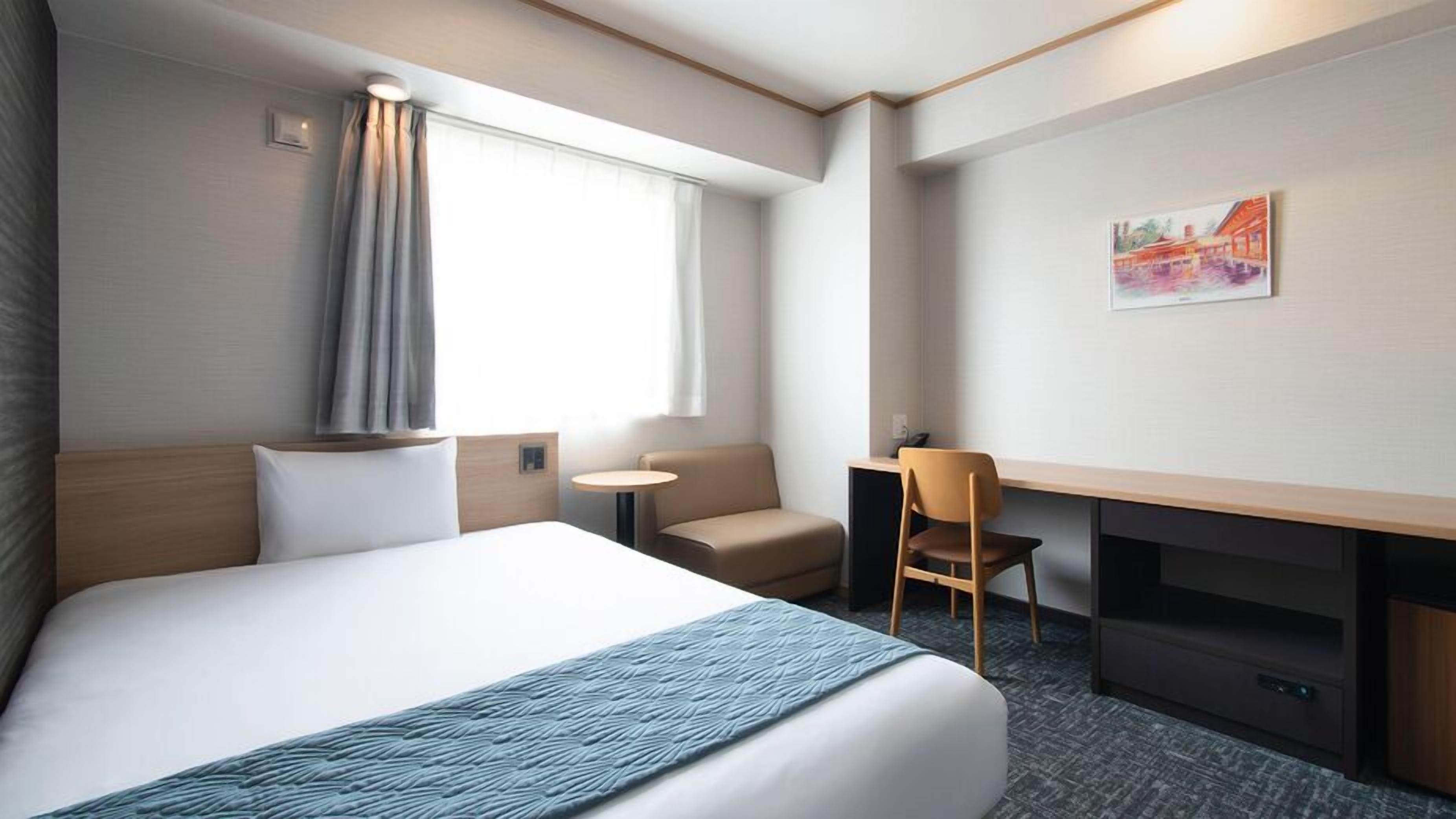 Ein Hotelzimmer mit Bett, Schreibtisch, Stuhl, kleinem Tisch und einem Bild an der Wand.