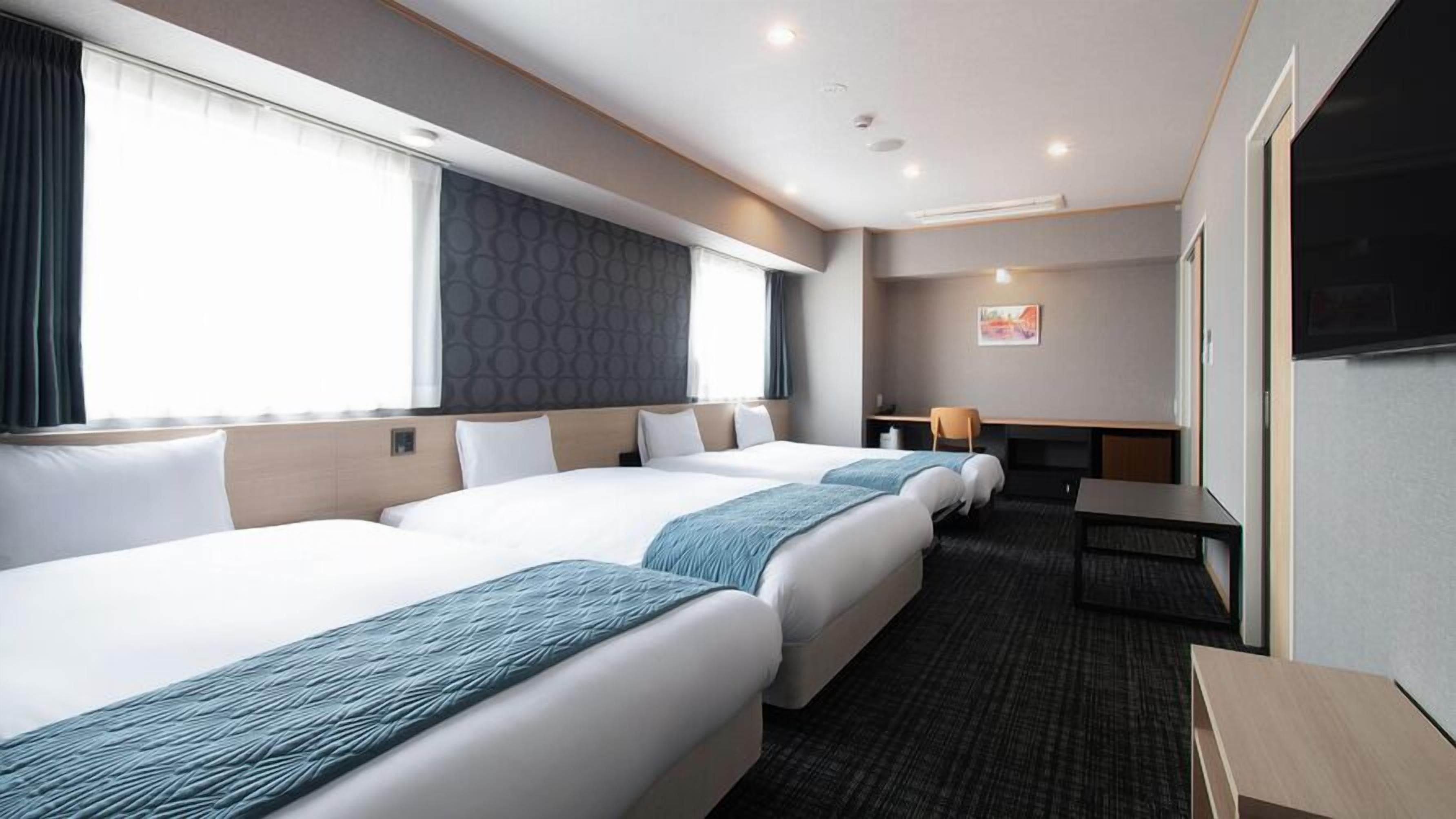 Ein Hotelzimmer mit drei Betten, einem Schreibtisch, einem Stuhl und einem Fernseher.