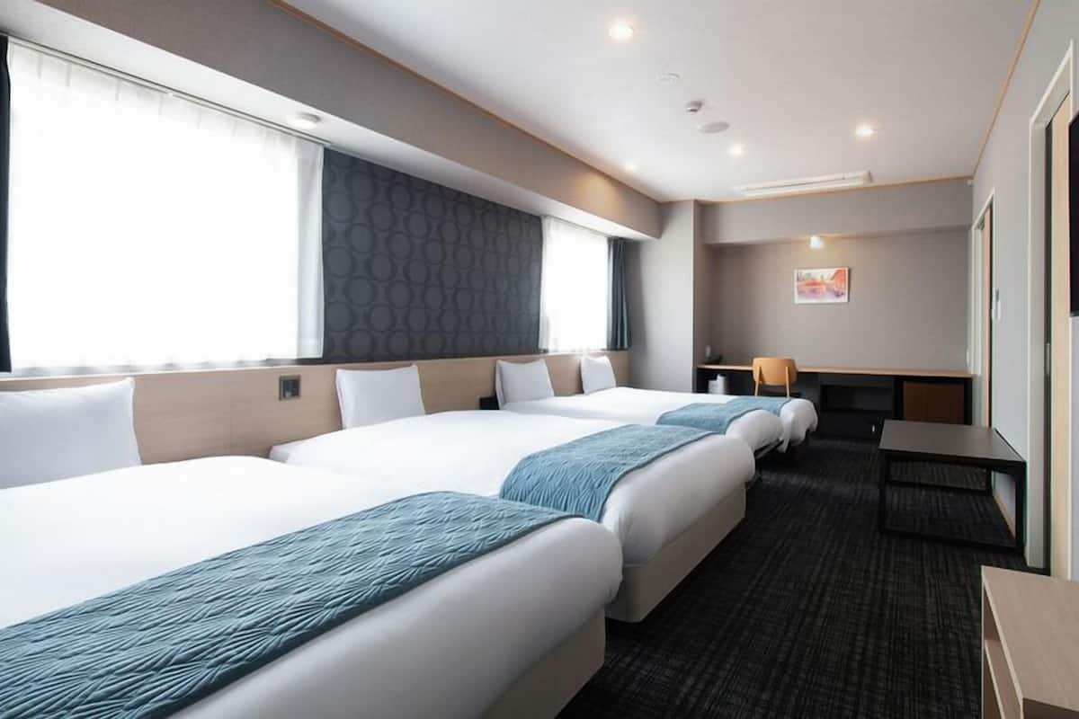 A hotel room with three beds, a desk, a chair, and a television.