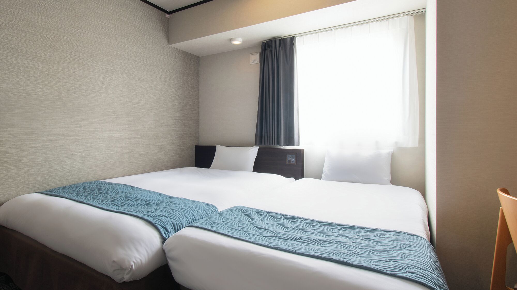 Ein Hotelzimmer mit zwei Betten, einem Fenster mit Vorhängen, einem Nachttisch und einem Sessel.
