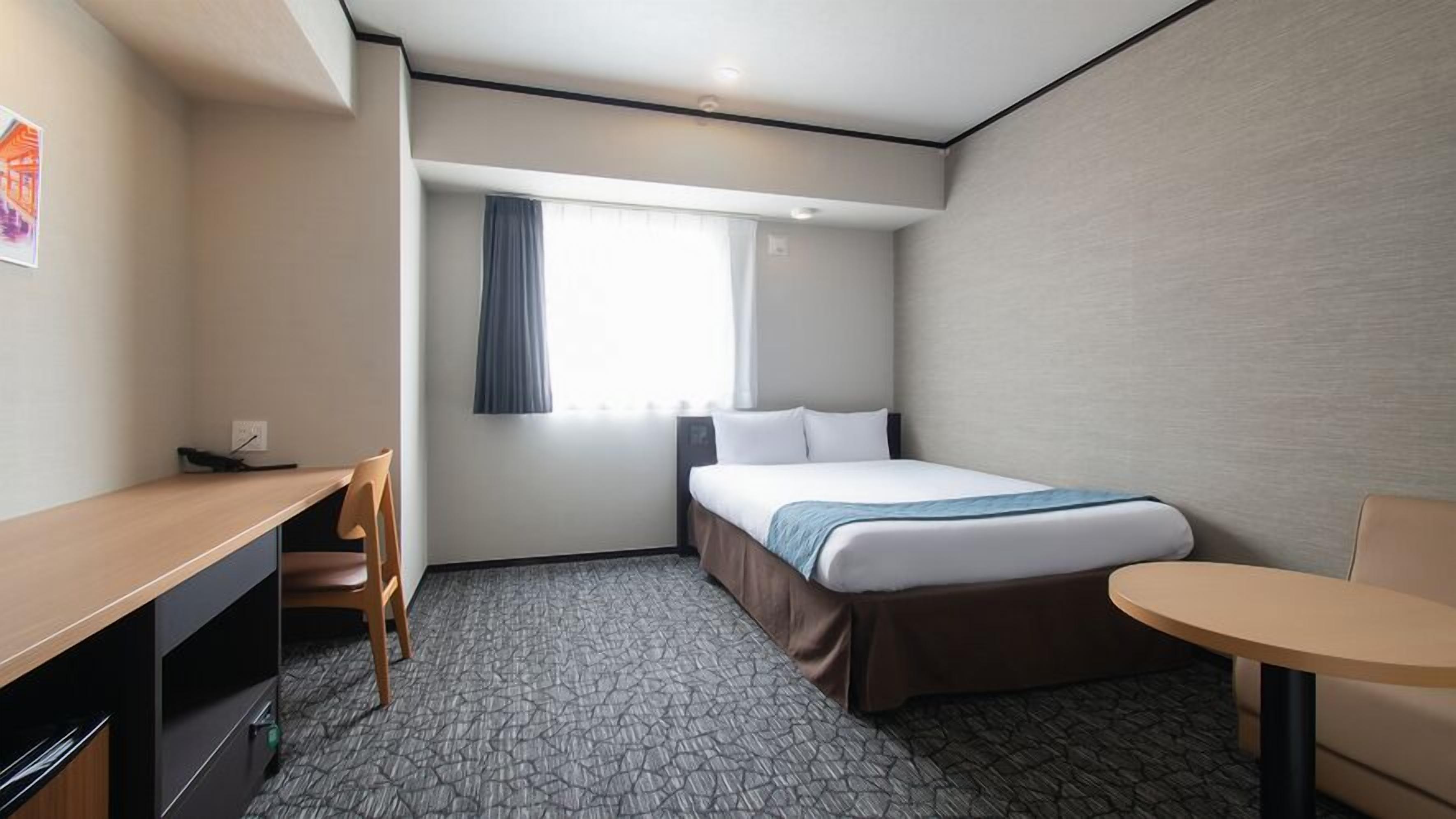 Ein Hotelzimmer mit Bett, Schreibtisch, Stuhl und einem kleinen Tisch.