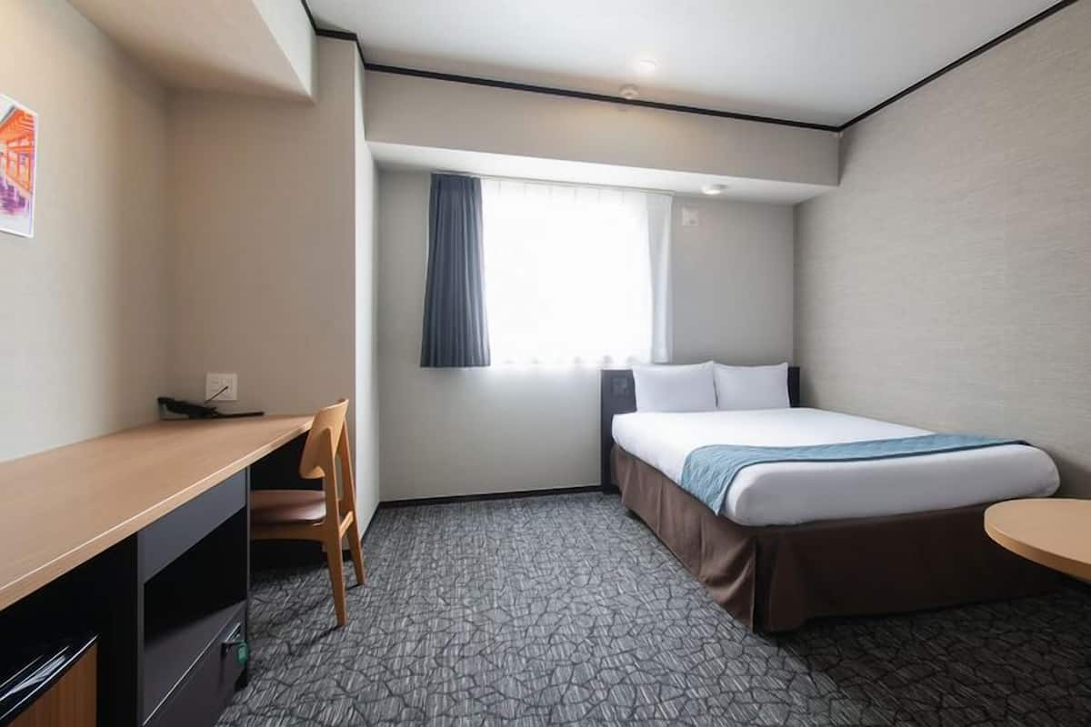 A hotel room with a bed, desk, chair, and a small table.