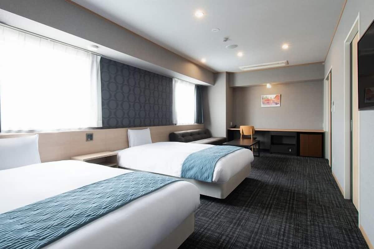 A hotel room with two beds, a desk, a chair, a TV, and a large window.