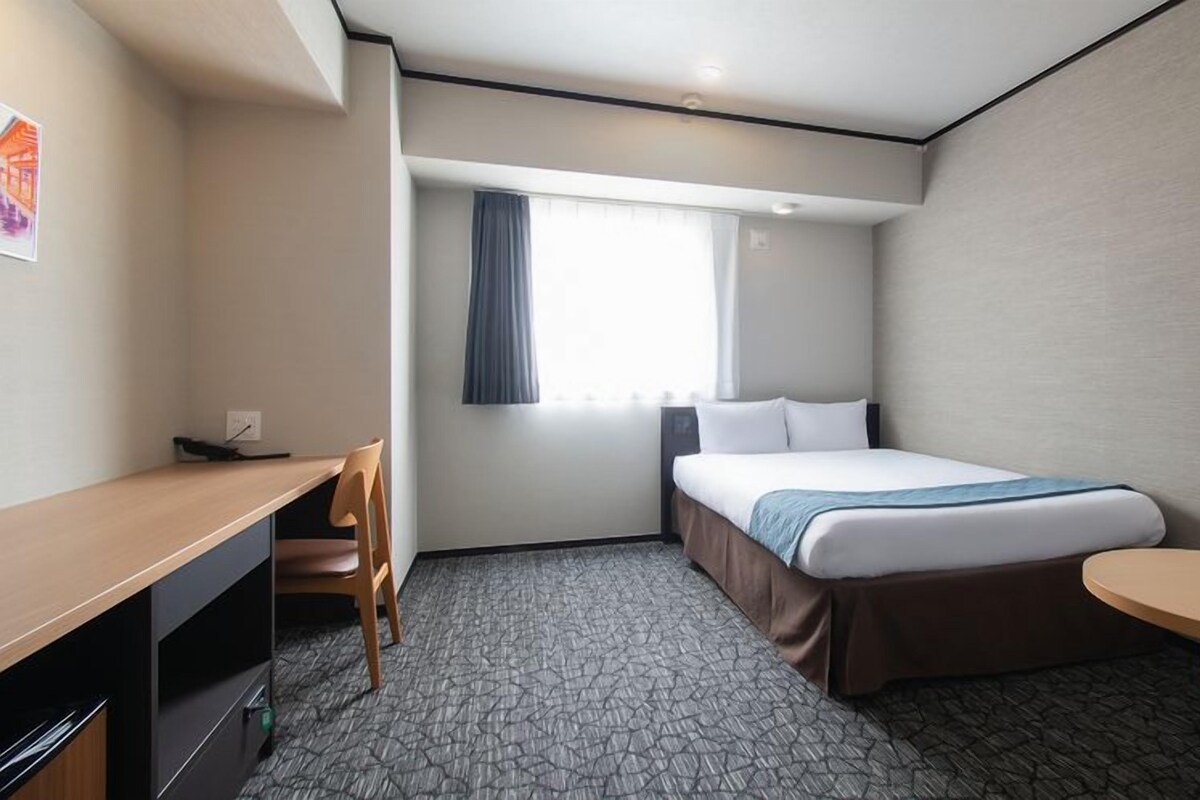 Une chambre d’hôtel avec un lit, un bureau, une chaise et une petite table.