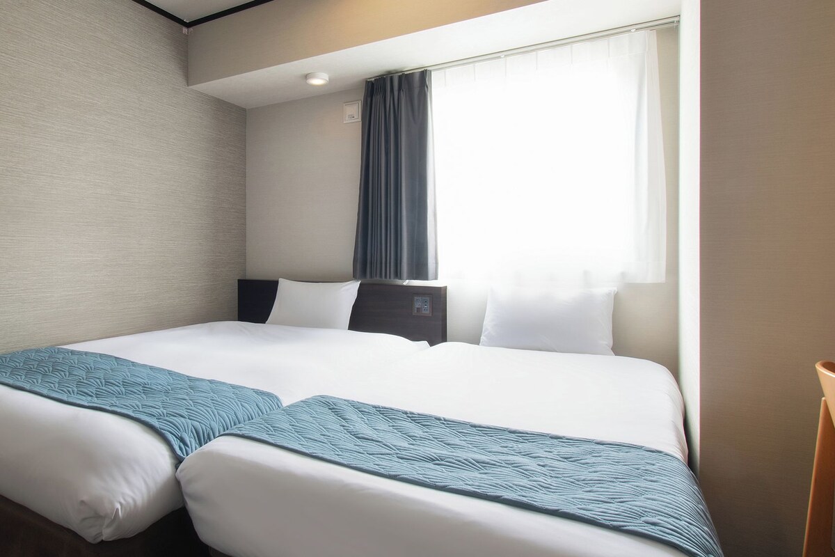 Een hotelkamer met twee bedden, een raam met gordijnen, een nachtkastje en een stoel.