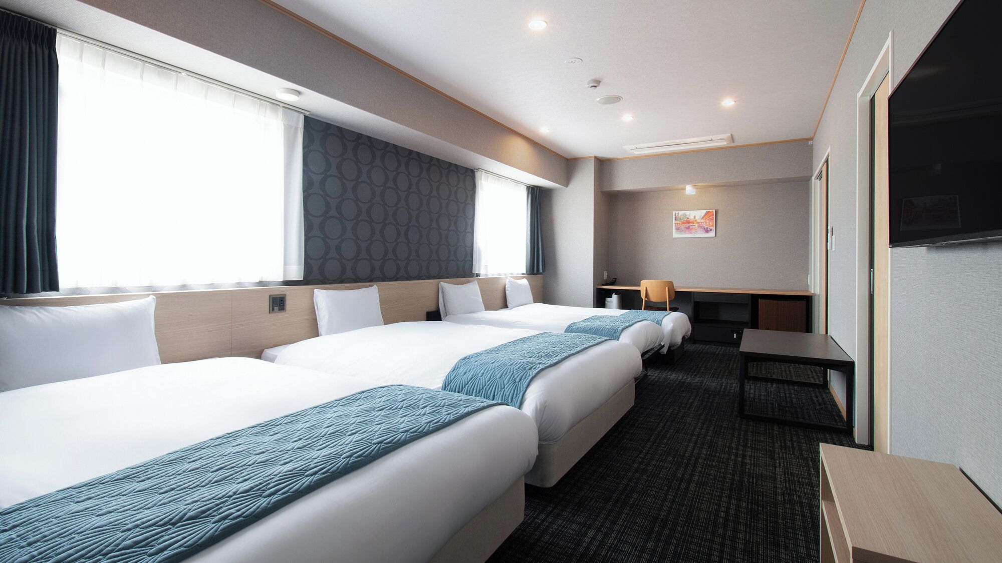 Ein Hotelzimmer mit zwei Betten, einem Schreibtisch, einem Stuhl, einem Fernseher und einem Fenster mit Vorhängen.