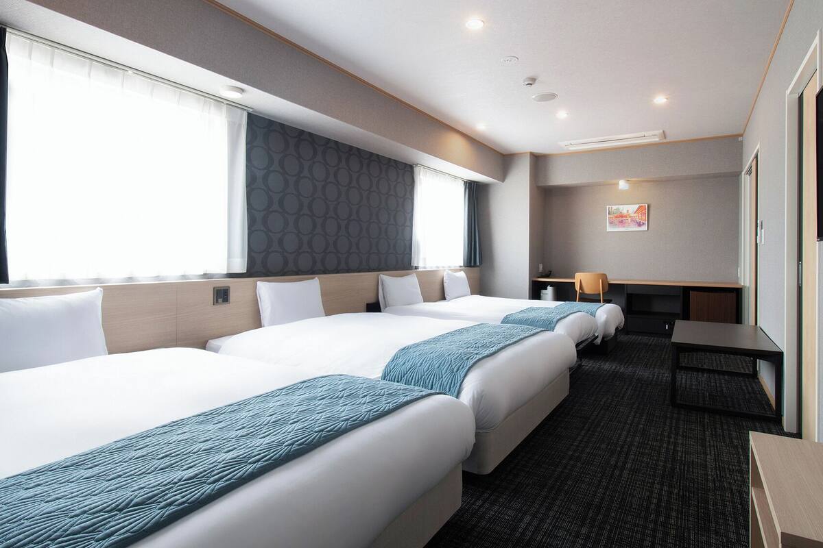 A hotel room with two beds, a desk, a chair, a TV, and a window with curtains.