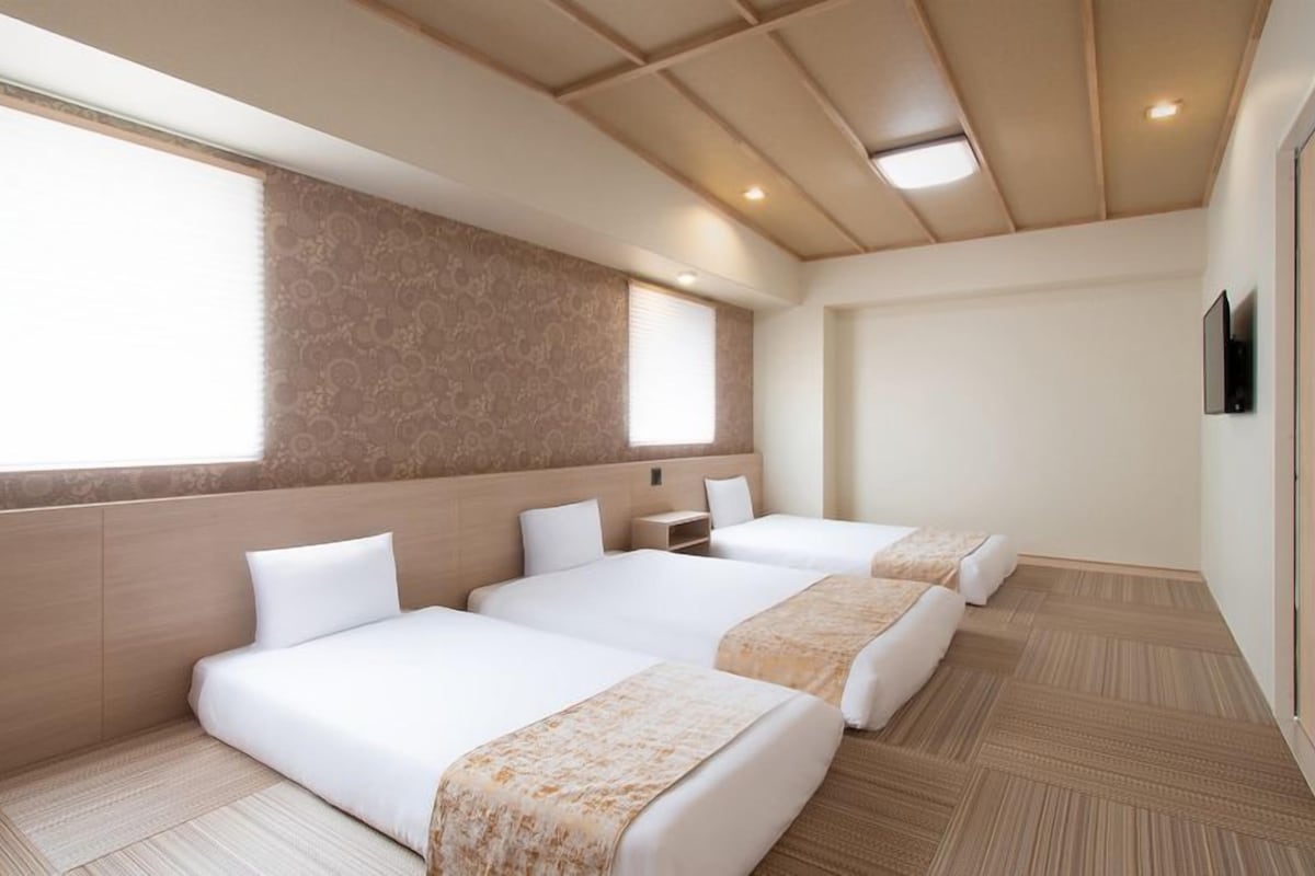 Habitación de hotel con tres camas, un ventanal grande y techo de madera.