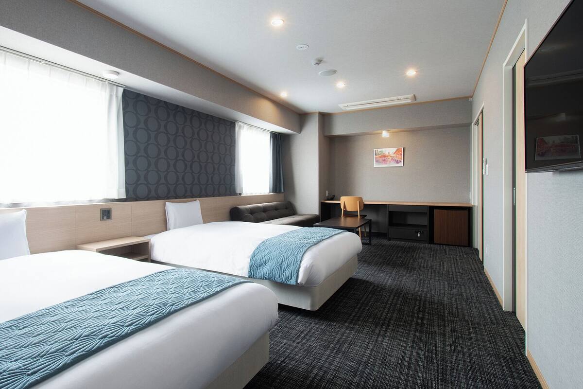 A hotel room with two beds, a desk, a chair, and a television.