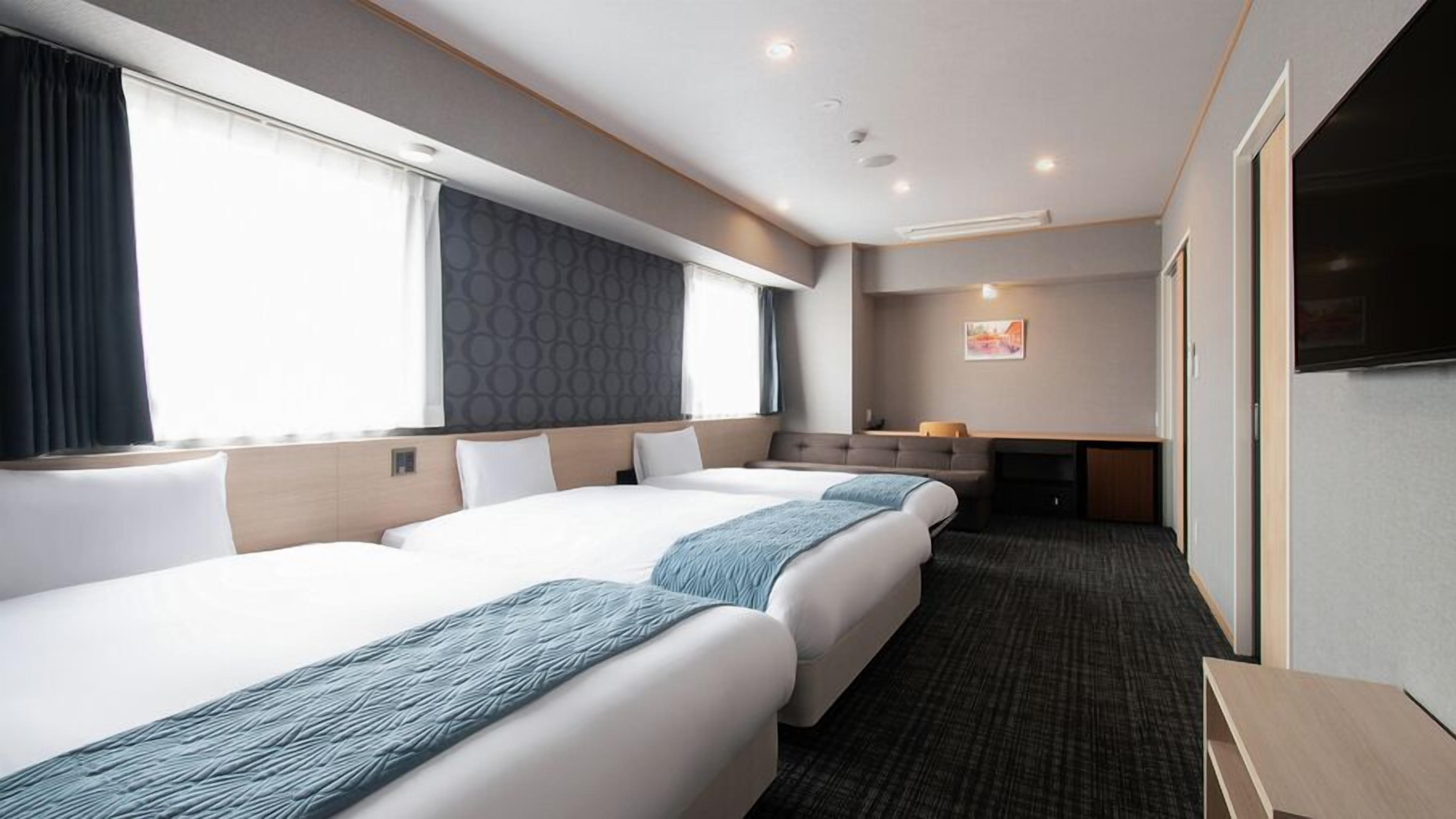 Ein Hotelzimmer mit drei Betten, einem Sofa, einem Schreibtisch und einem Fernseher.