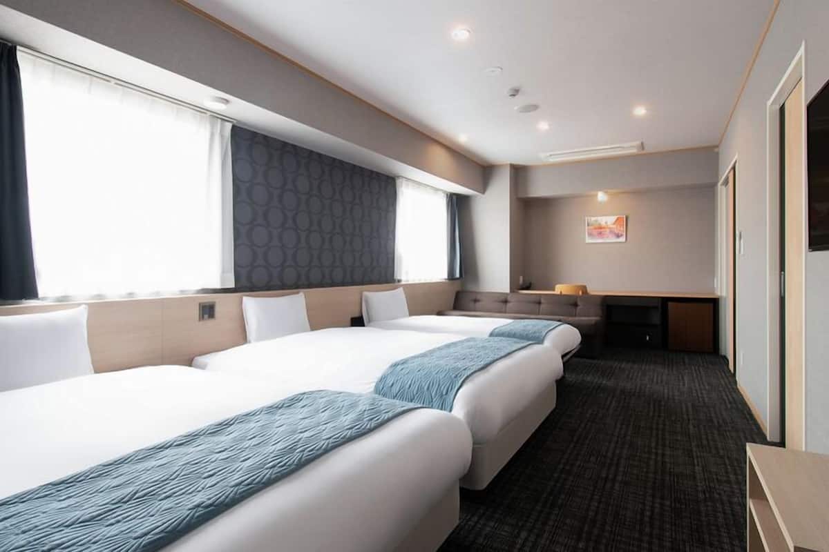 A hotel room with three beds, a sofa, a desk, and a TV.