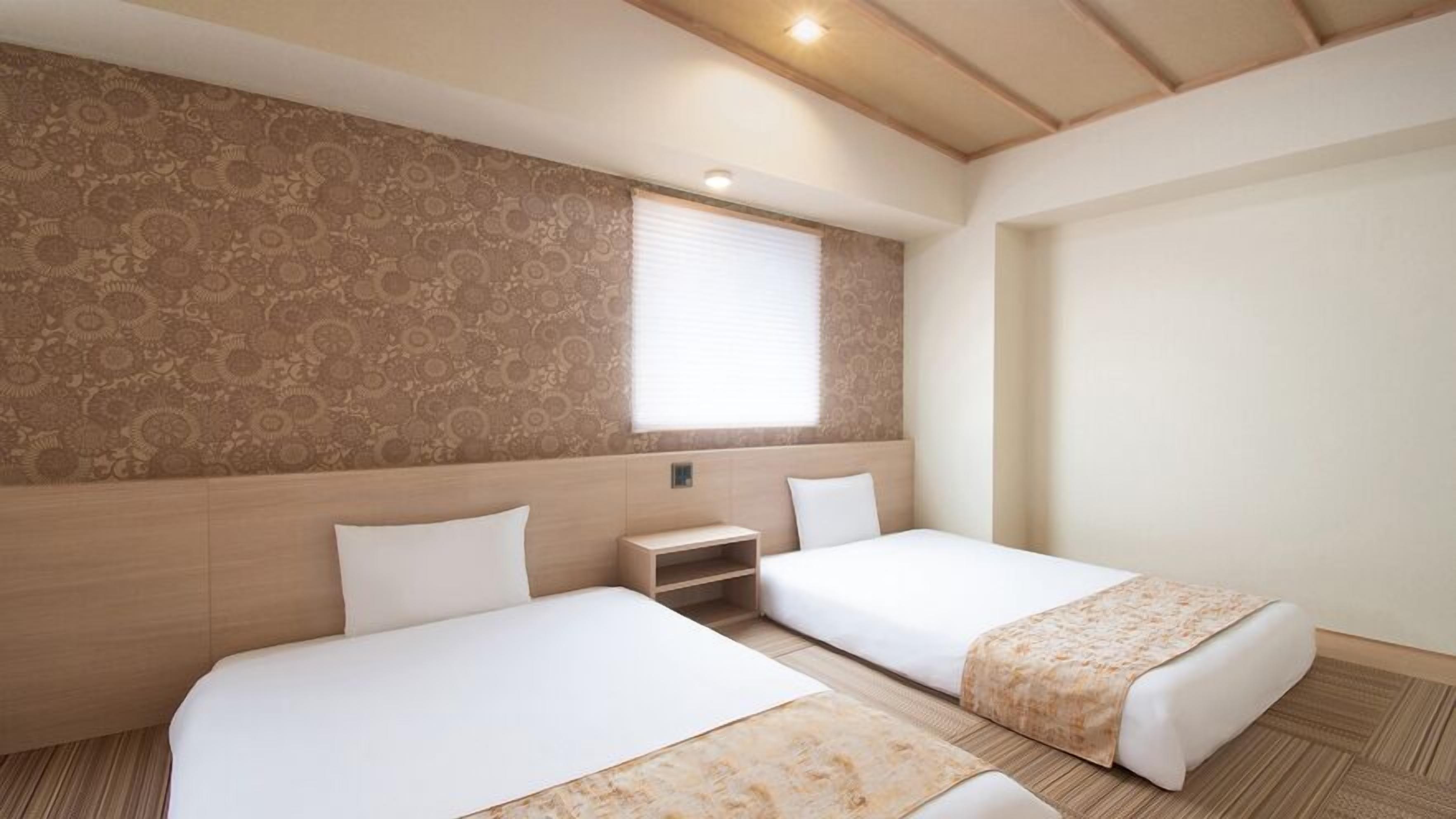 Ein Hotelzimmer mit zwei Betten, einem kleinen Nachttisch, einem Fenster mit Jalousien und einer Wand mit Muster.
