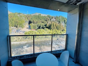 A room with a large window overlooking a river and a forested hillside. - Hida-kanayama Nukumori-no-sato Onsen (Gero)